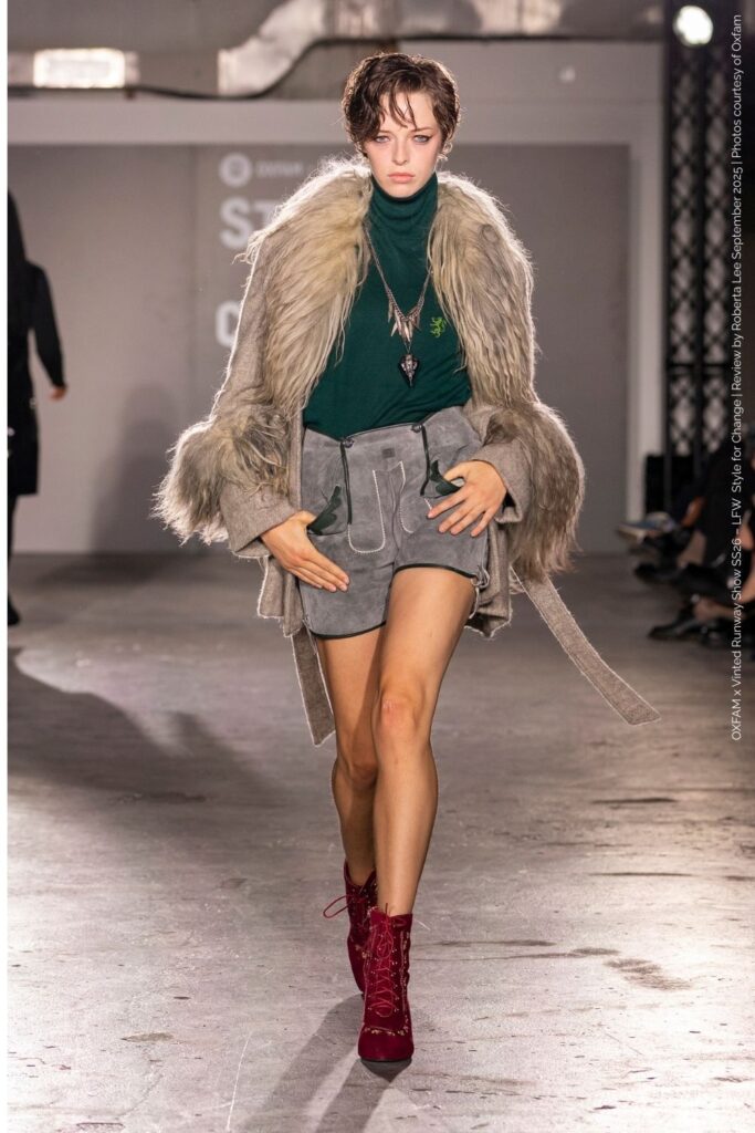 Cassidy Clover preloved look at LFW.   wearing grey shorts, green top, red boots and fur coat at the Oxfam Runway Show LFW SS26.”